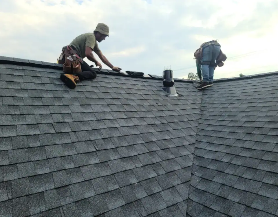 Two workers wearing tool belts are on a shingled roof, performing repairs or installation work near the roof ridge beneath a partly cloudy sky—expert service from a trusted Home Remodeling Union County, NJ team.