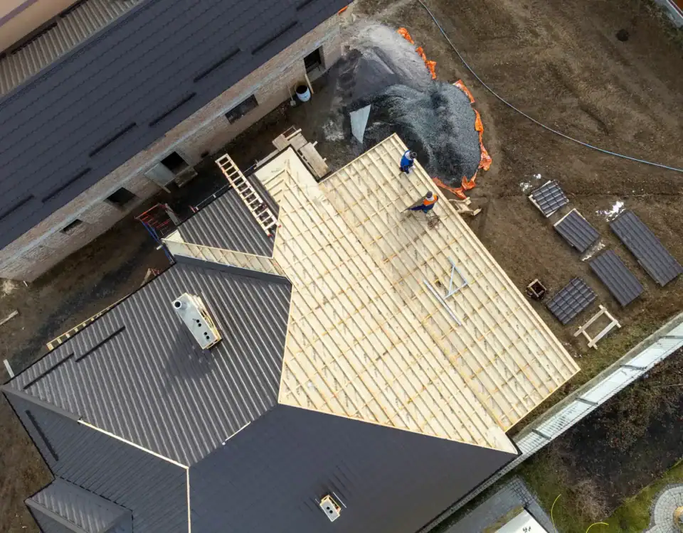 Aerial view of a house under construction in NJ, showing workers installing a wooden roof frame, building materials, and roofing sheets scattered nearby—an example of quality Home Remodeling Union County professionals deliver.