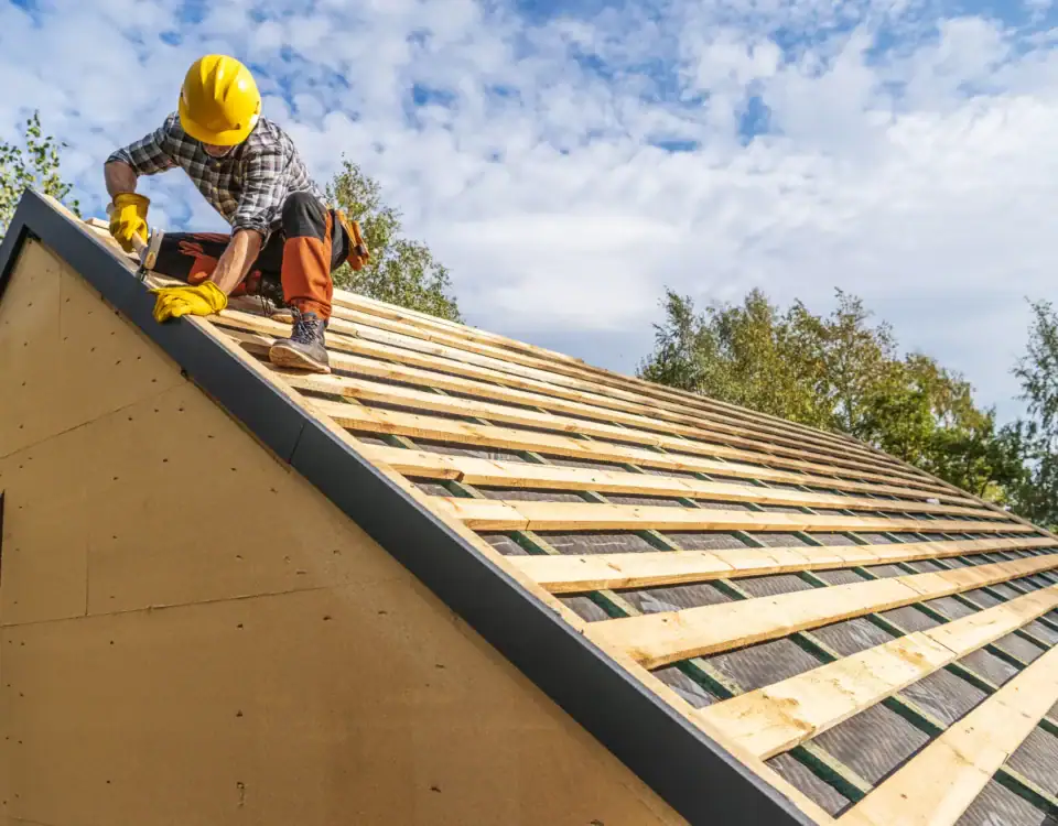A construction worker wearing a yellow hard hat and gloves installs wooden planks on a sloped roof of a house under construction in Union County, NJ, showcasing the quality craftsmanship typical of home remodeling projects.