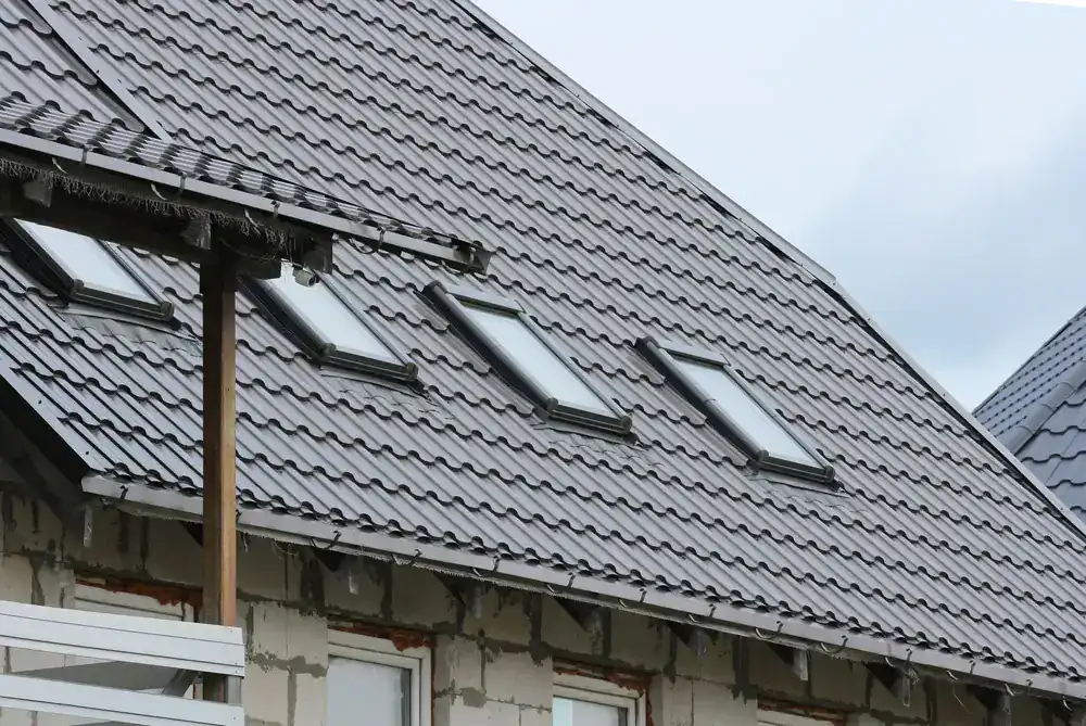 Close-up of a house in NJ with a sloped roof covered in dark gray metal roofing tiles and several rectangular skylight windows, showcasing ongoing Roofing Services Union County during construction or renovation.